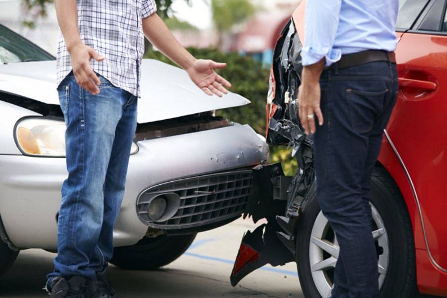 Two people standing beside their cars after a collision, discussing the front-end damage.